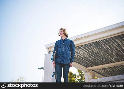 Portrait of young male urban skateboarder holding skateboard