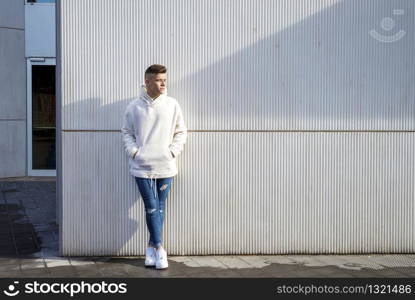 Portrait of young male with hands on pocket leaning on pole outdoors