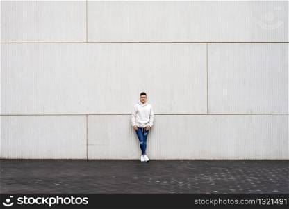 Portrait of young male with hands on pocket leaning on wall outdoors