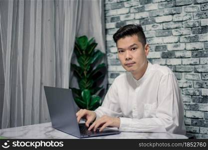Portrait of young man businessman working at office with laptop on desk, looking at camera, smiling.
