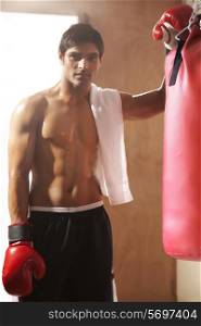 Portrait of young man by punching bag at gym