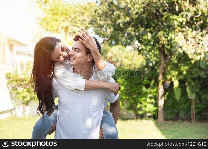 Portrait of young man carrying his beautiful asian woman on his back at park, Boyfriend giving piggyback ride to his beautiful girlfriend in summer holiday.Romantic and enjoying in summer holiday.