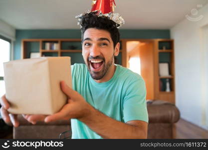 Portrait of young man celebrating his birthday on a video call and opening presents while staying at home. New normal lifestyle concept.. Man celebrating his birthday on a video call.