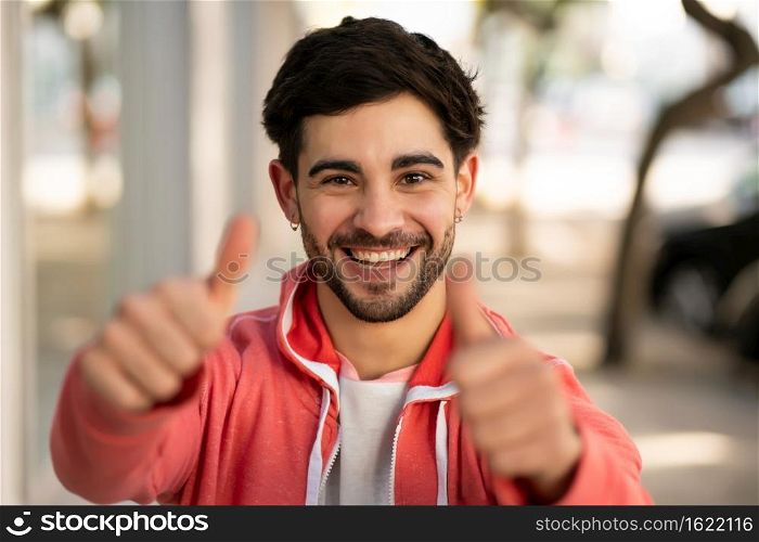 Portrait of young man celebrating victory while standing outdoors at the street. Urban and success concept.