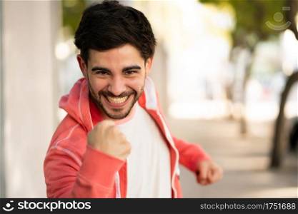Portrait of young man celebrating victory while standing outdoors at the street. Urban and success concept.