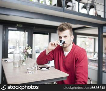 Portrait of young man drinking espresso in cafe