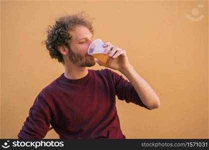 Portrait of young man enjoying and drinking beer against yellow background. Lifestyle concept.