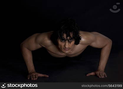 Portrait of young man exercising against black background