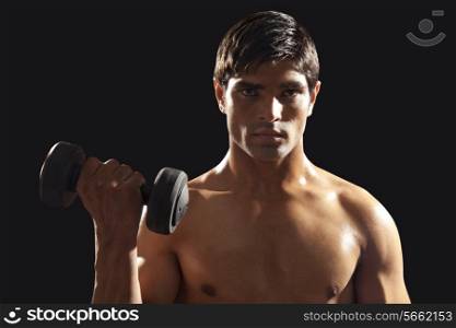 Portrait of young man exercising with dumbbell isolated over black background