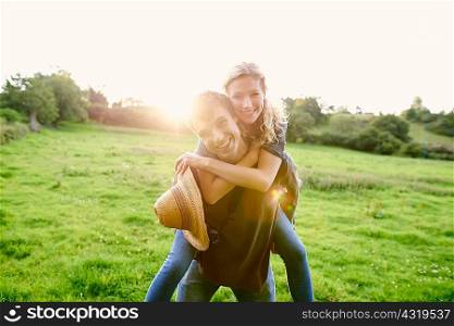 Portrait of young man giving girlfriend a piggyback in rural field