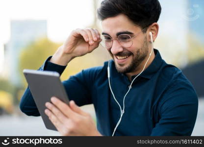 Portrait of young man having a video call on digital tablet while standing on bench outdoors. Urban concept.