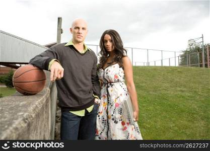 Portrait of young man holding a basketball and young woman holding a laptop computer standing next to each other