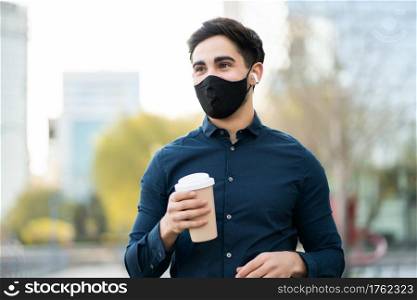 Portrait of young man holding a cup of coffee while standing outdoors on the street. New normal lifestyle concept. 