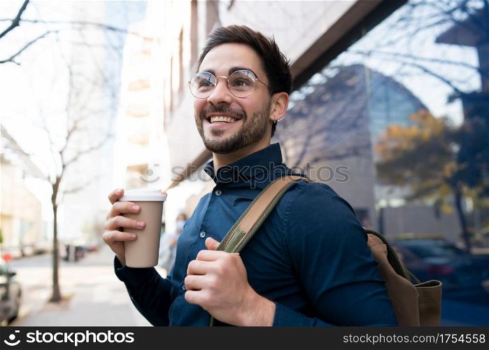 Portrait of young man holding a cup of coffee while walking outdoors at the street. Urban and lifestyle concept.