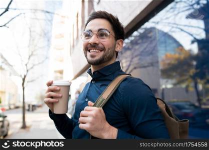 Portrait of young man holding a cup of coffee while walking outdoors at the street. Urban and lifestyle concept.