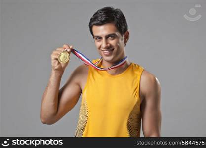 Portrait of young man holding gold medal isolated over gray background