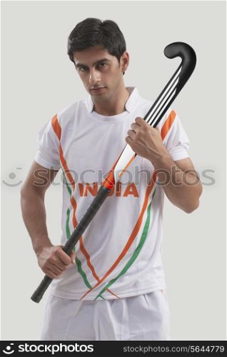 Portrait of young man holding hockey stick against gray background