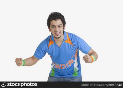 Portrait of young man in Indian cricket team jersey cheering with clenched fists over white background