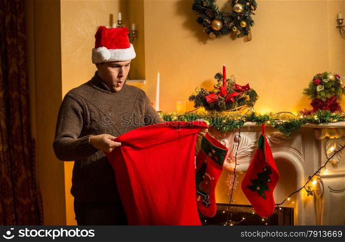 Portrait of young man in red hat looking inside of Santa bag with amazement