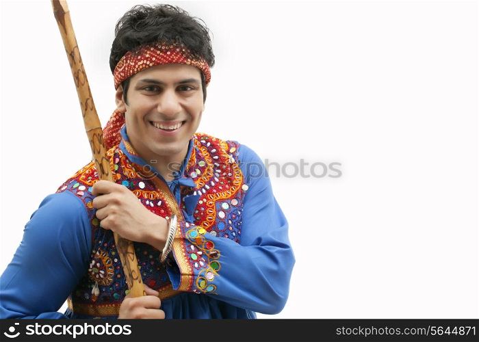 Portrait of young man in traditional wear holding stick against white background