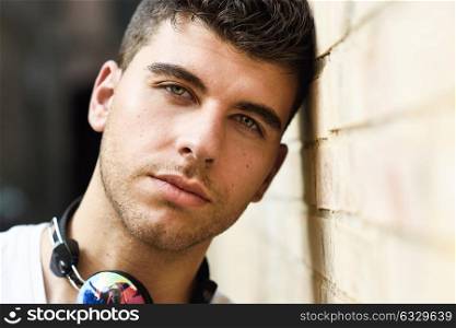 Portrait of young man in urban background listening to music with headphones. Wearing white t-shirt near a brick wall
