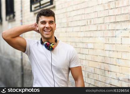 Portrait of young man in urban background listening to music with headphones. Wearing white t-shirt near a brick wall