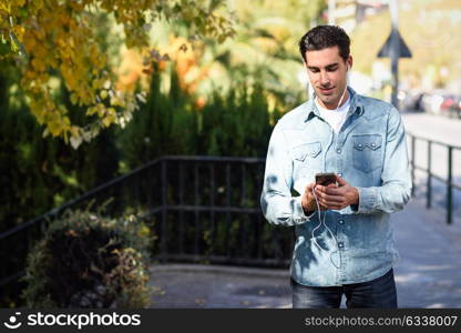 Portrait of young man in urban background listening to music with headphones. Guy wearing casual clothes with a smartphone.