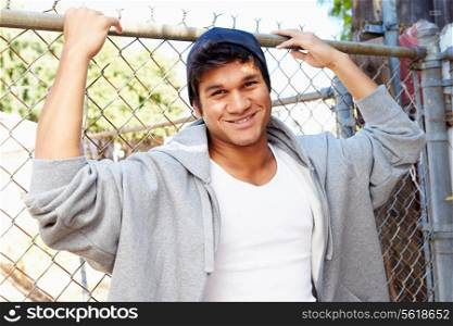 Portrait Of Young Man In Urban Setting Standing By Fence