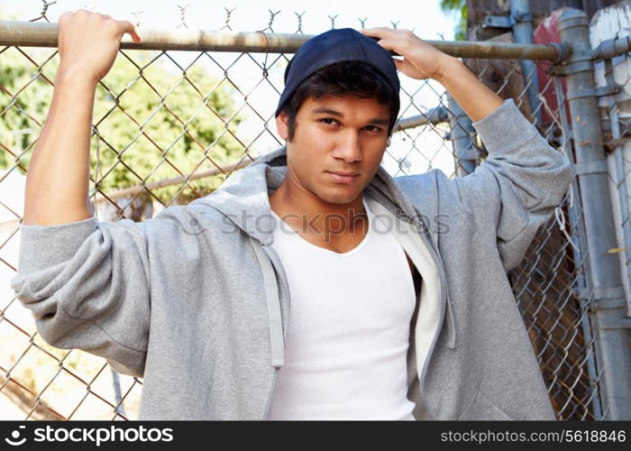 Portrait Of Young Man In Urban Setting Standing By Fence