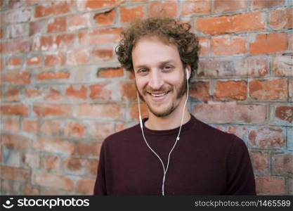 Portrait of young man listening to music with earphones against brick wall. Urban concept.