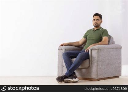 Portrait of young man looking at camera while sitting on sofa