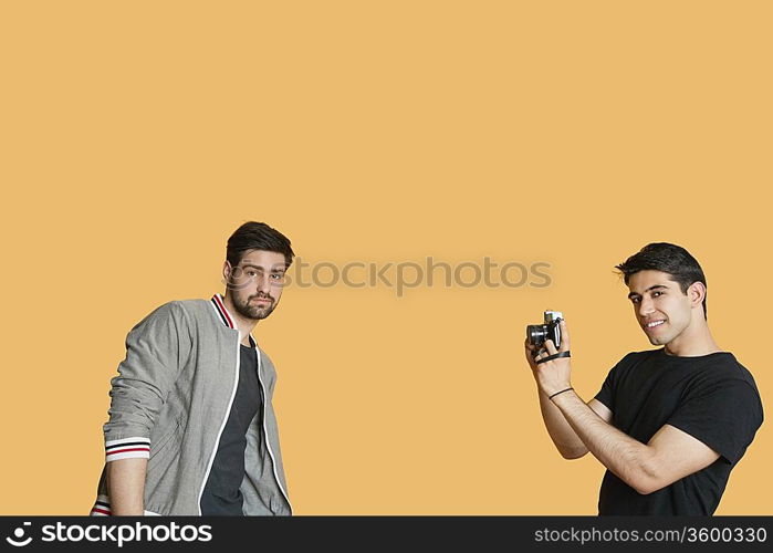 Portrait of young man photographing friend over colored background