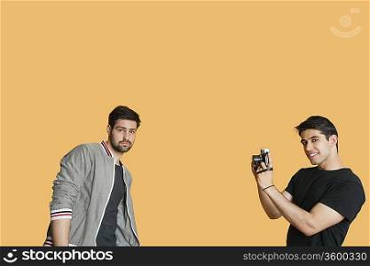 Portrait of young man photographing friend over colored background