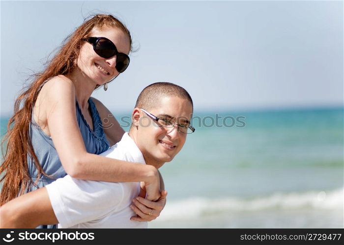 Portrait of Young man piggyback his girlfriend on the beach