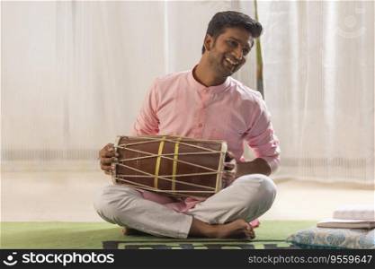 Portrait of young man playing Dholak at home