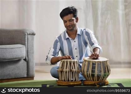 Portrait of young man playing Tabla at home