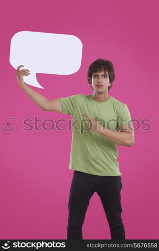 Portrait of young man pointing at speech bubble over pink background