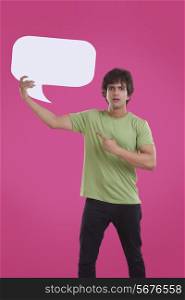 Portrait of young man pointing at speech bubble over pink background