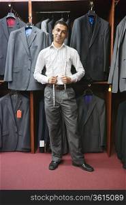 Portrait of young man posing with suits hanging in background