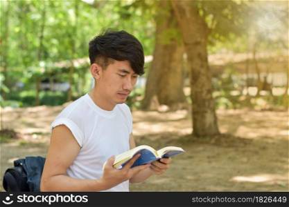 Portrait of young man reading a book in the park on summer day.
