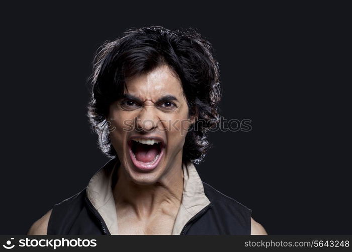 Portrait of young man screaming against black background