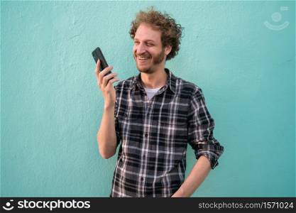 Portrait of young man sending voice message with his mobile phone against blue background. Communication concept.