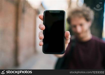 Portrait of young man showing blank smartphone screen and looking at the camera. Promoting and advertising concept.