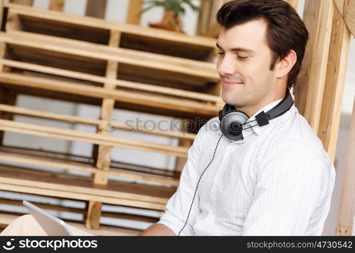 Portrait of young man sitting at the stairs in office. Portrait of young businessman sitting at the stairs in office with headphones