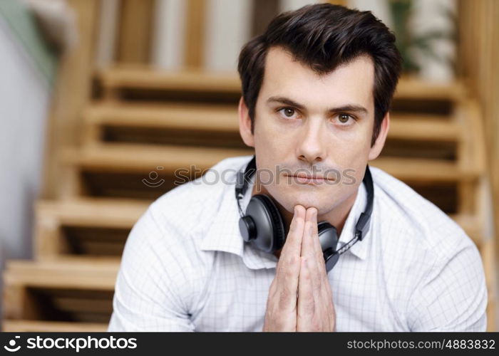 Portrait of young man sitting at the stairs in office. Portrait of young businessman sitting at the stairs in office with headphones