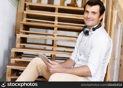 Portrait of young man sitting at the stairs in office. Portrait of young businessman sitting at the stairs in office with headphones