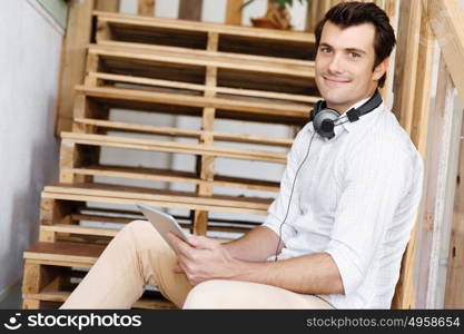 Portrait of young man sitting at the stairs in office. Portrait of young businessman sitting at the stairs in office with headphones