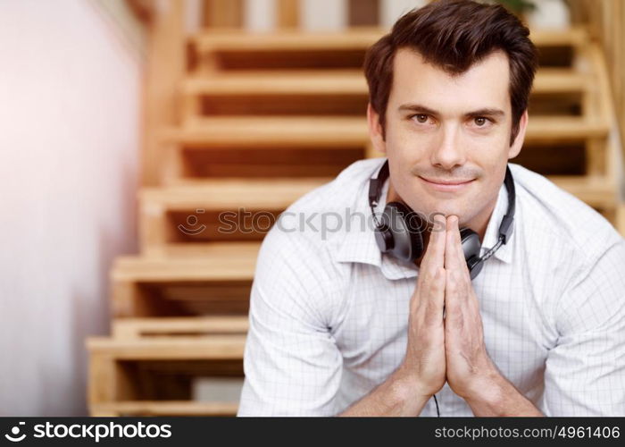 Portrait of young man sitting at the stairs in office. Portrait of young businessman sitting at the stairs in office with headphones