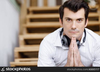 Portrait of young man sitting at the stairs in office. Portrait of young businessman sitting at the stairs in office with headphones