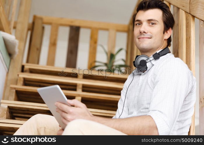 Portrait of young man sitting at the stairs in office. Portrait of young businessman sitting at the stairs in office with headphones